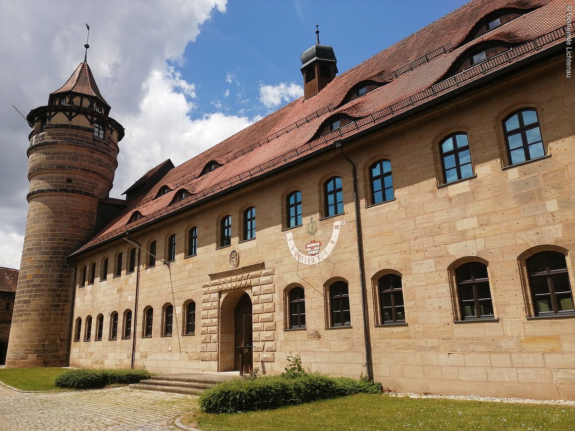 Historisches Gebäude mit Turm und Sonnenuhr, blauer Himmel und Wolken im Hintergrund.