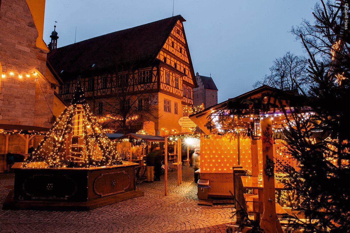 Weihnachtsmarkt mit beleuchteten Ständen und Fachwerkhaus im Hintergrund bei Dämmerung.