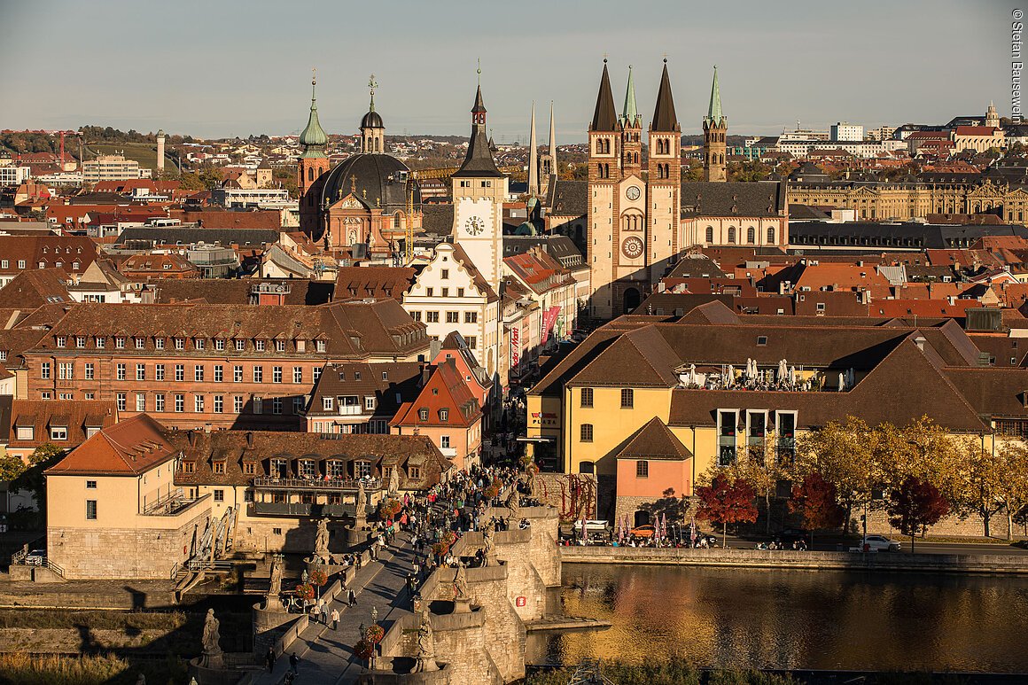 Stadtansicht mit Brücke, Fluss, historischen Gebäuden und Kirchtürmen im Hintergrund bei Tageslicht.