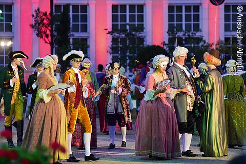 Personen in historischen Kostümen und Masken bei einer Veranstaltung im Freien.