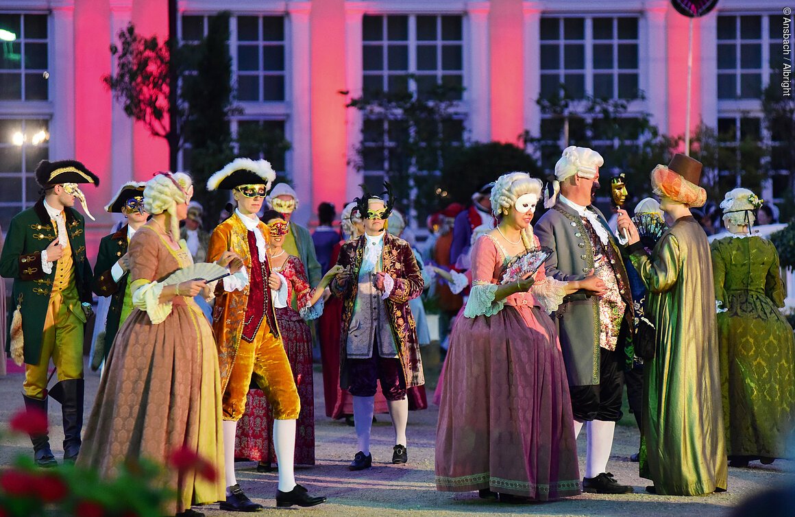 Personen in historischen Kostümen und Masken bei einer Veranstaltung im Freien.